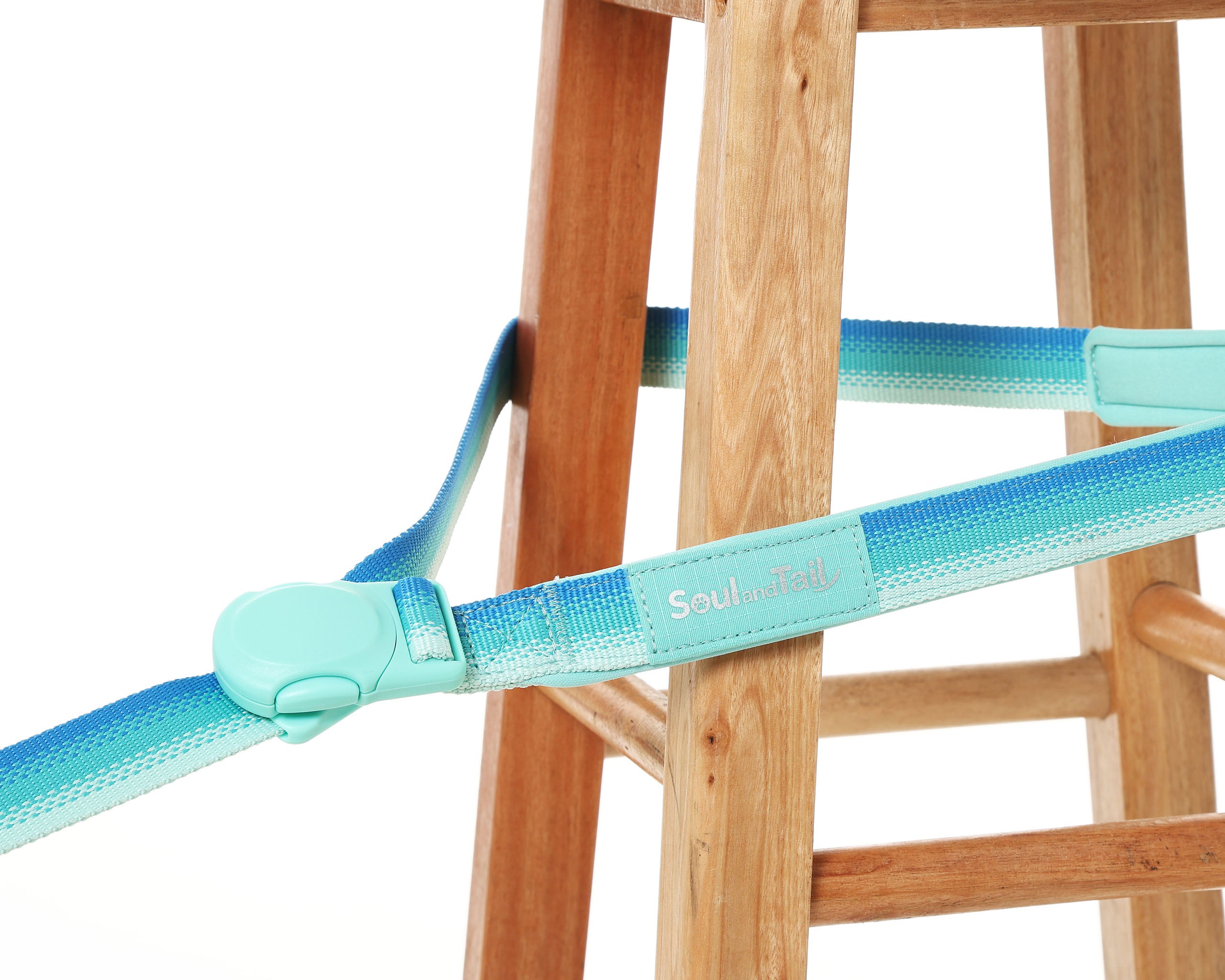 Turquoise dog leash with gradient design attached by a magnetic buckle to a wooden stool on a white background