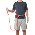 Person wearing an orange belt with a magnetic buckle, holding an aluminum carabiner on the end of the orange leash, on a white background