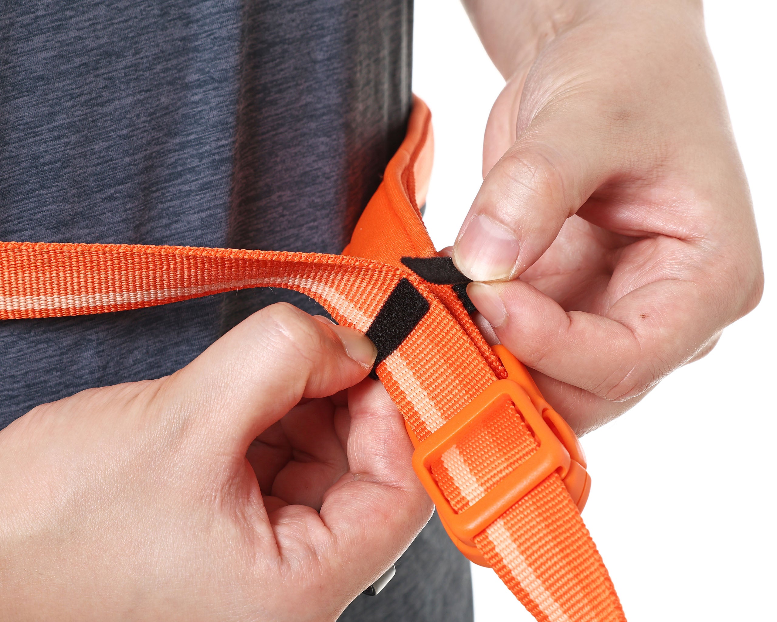 Person adjusting an orange belt with a black velcro on a plain background