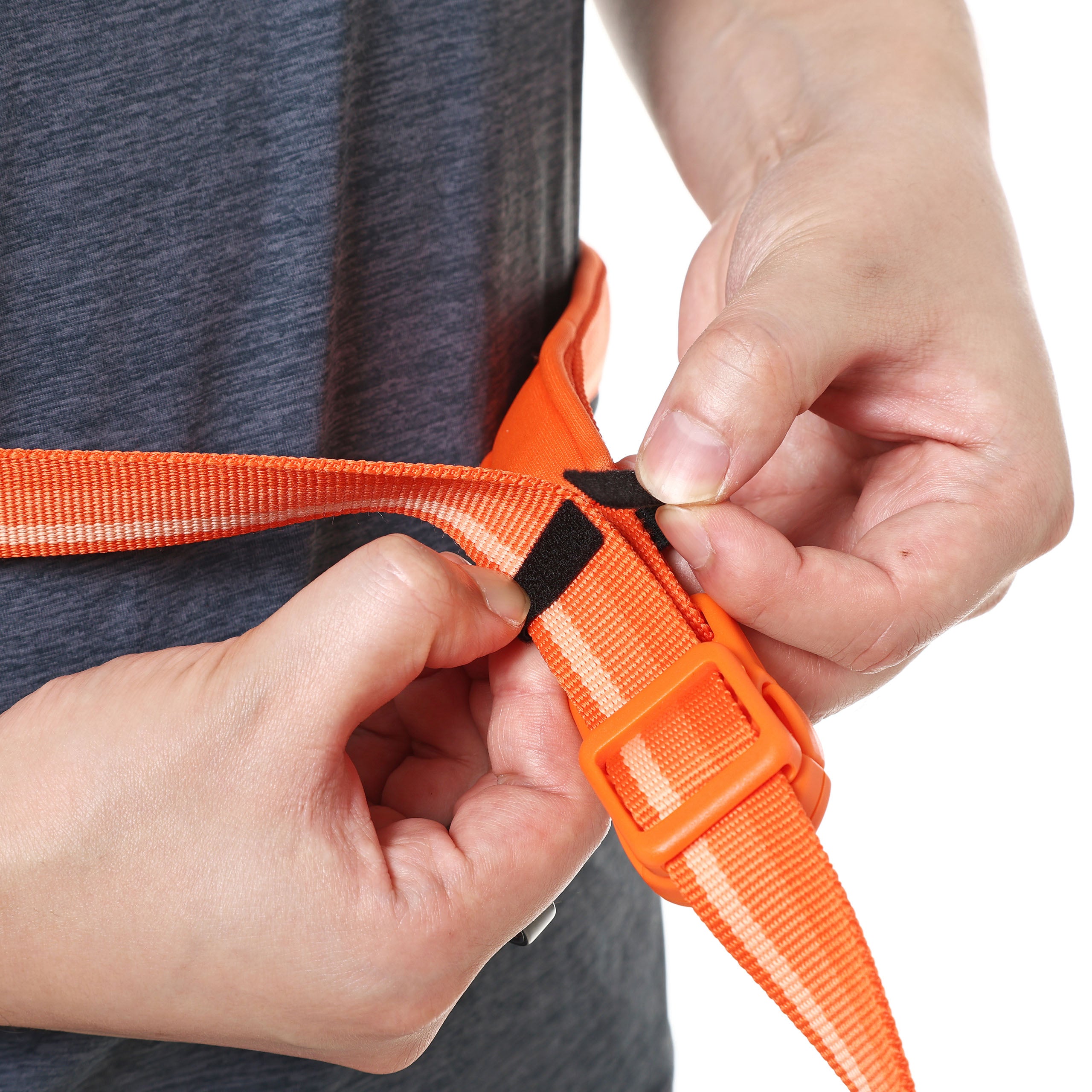 Person adjusting an orange belt with a black velcro on a plain background
