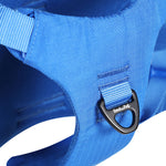 Close-up of a blue dog harness with a brand logo on a black, anodized, polished aluminum ring on a white background