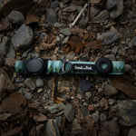 A green Forest Mist patterned dog collar on a rocky ground with leaves