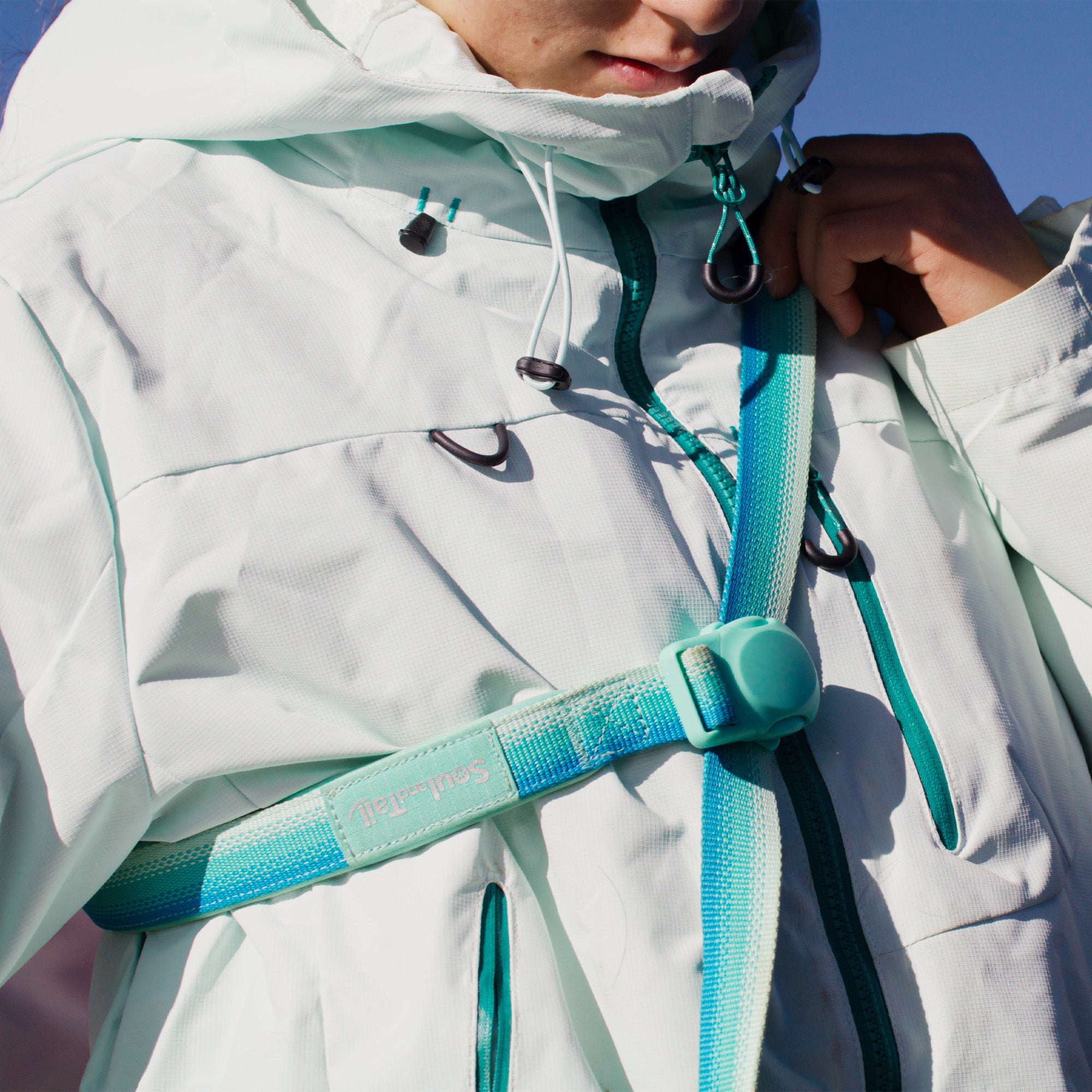 A woman wearing a mint colored coat, using an aqua coast color dog leash in crossbody style, with the mint green magnetic buckle in the center of the image