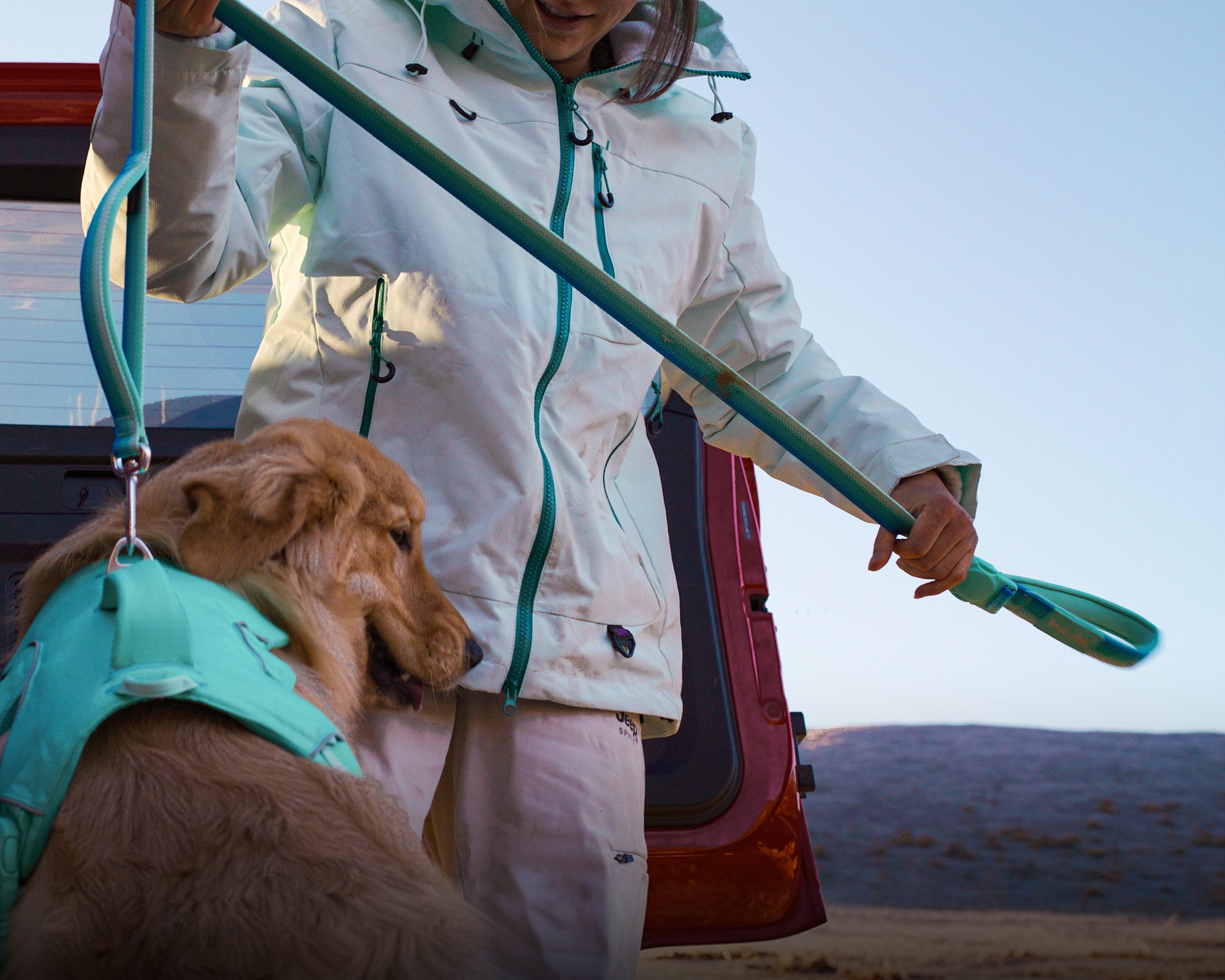 A woman in a mint color coat using a leash attached to a mint green harness worn by a dog