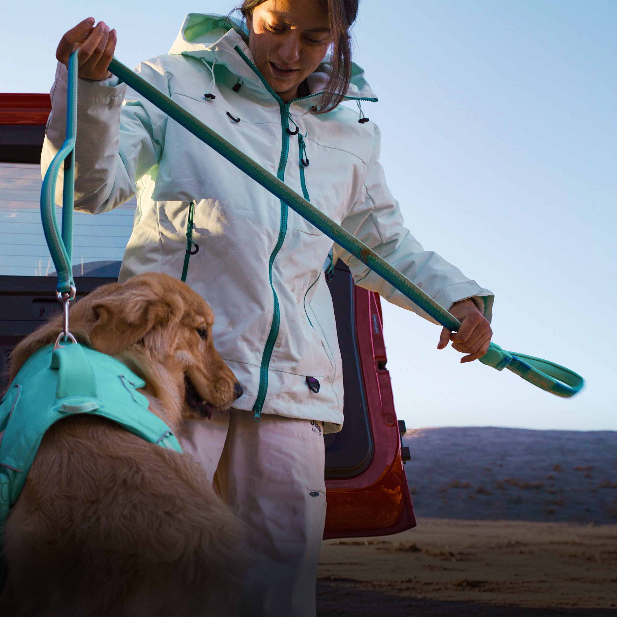 A woman in a mint color coat using a leash attached to a mint green harness worn by a dog