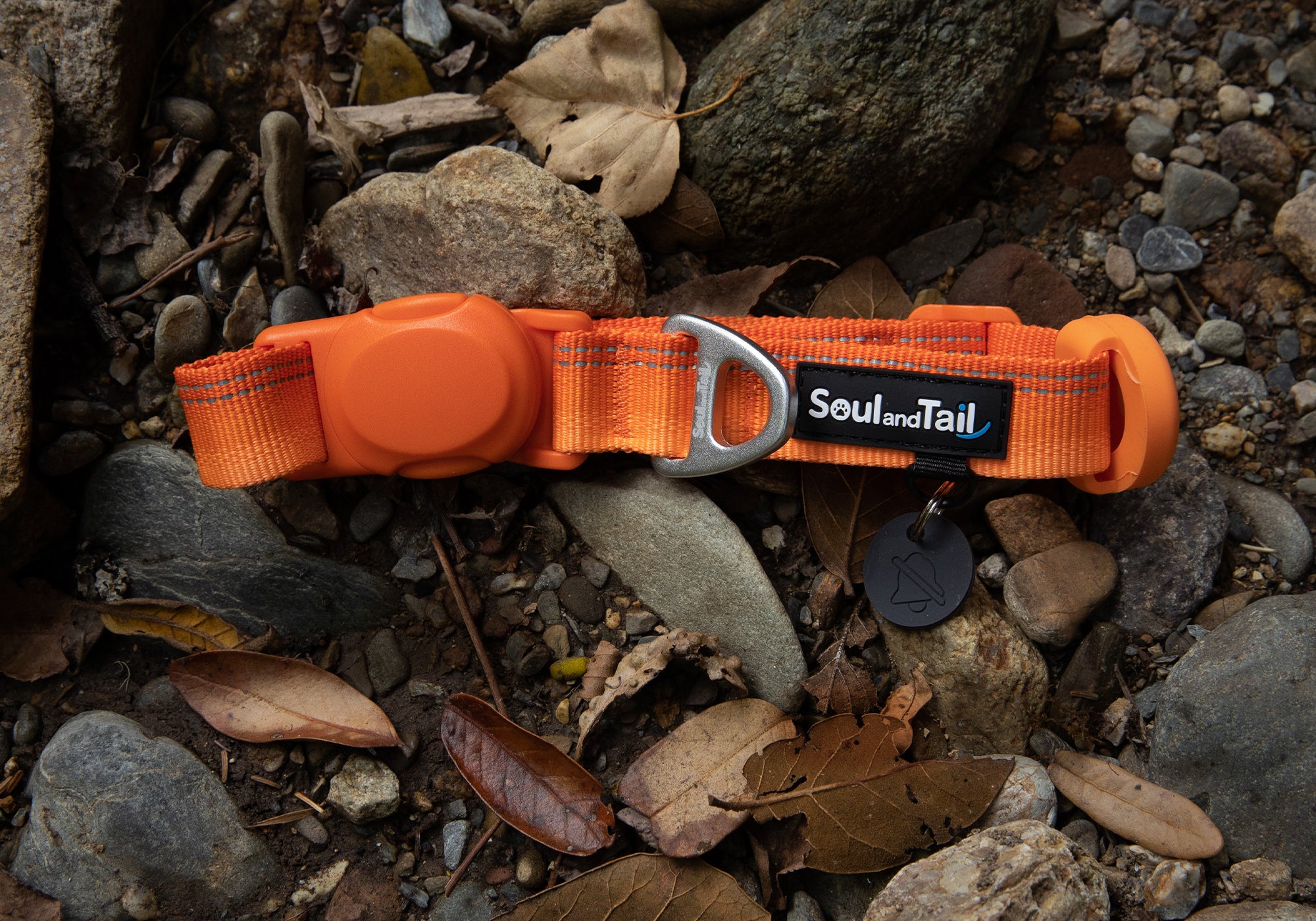 Orange dog collar with a "Soul and Tail" brand tag on a rocky ground